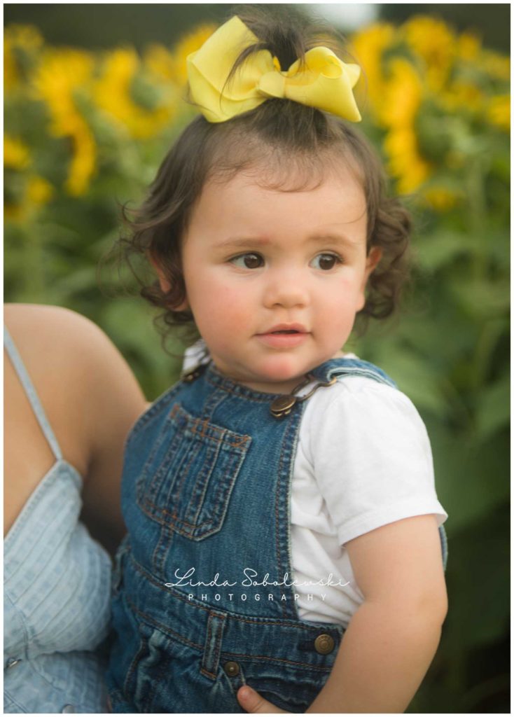 baby with yellow bow in field of sunflowers