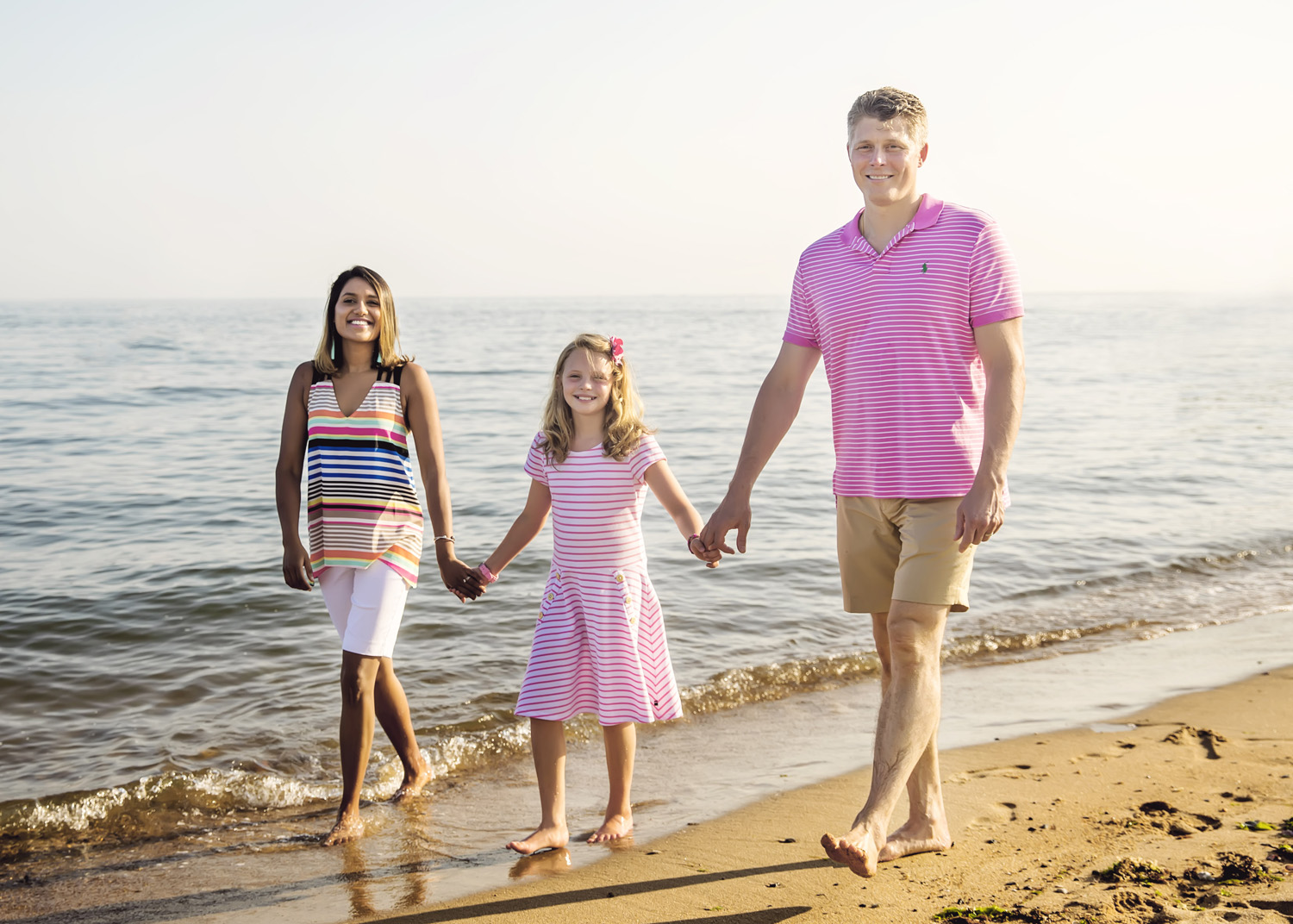family of three holding hands walking along the beach