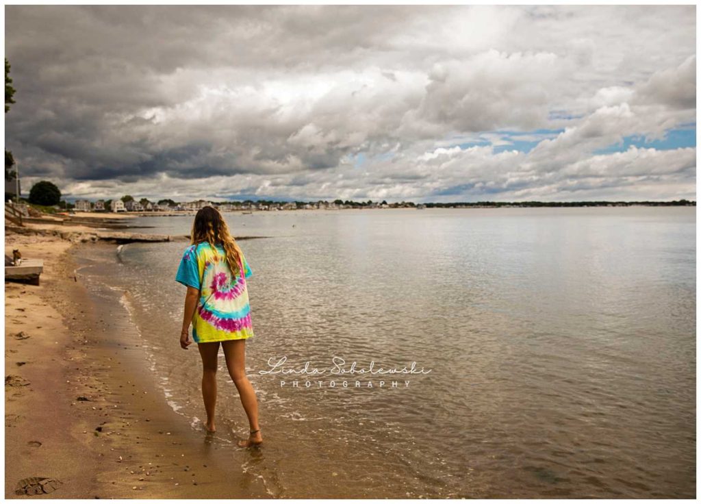 girl in tie-dye shirt walking on the beach with storm clouds 100 days of summer project
