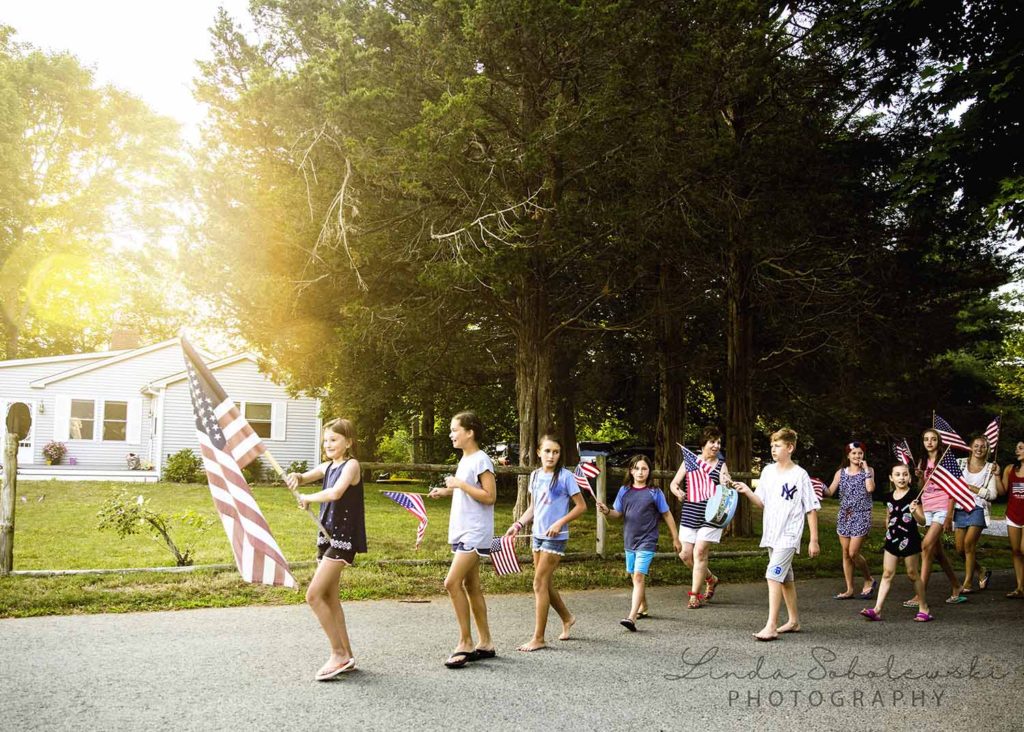 children walking down the street carrying the American flag on the 4th of July, Westbrook family photographer
