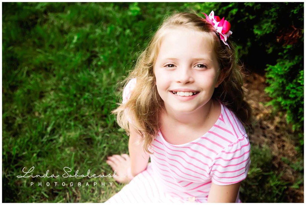 pretty lttle girl with blonde hair and pink bow smiling, extended family session