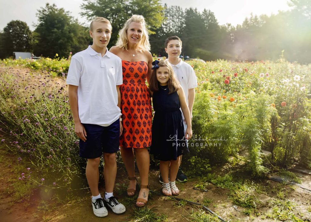 family of four smiling in field of flowers