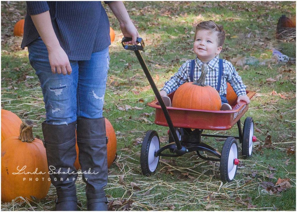 mom pulling baby boy in red wagon with pumpkin