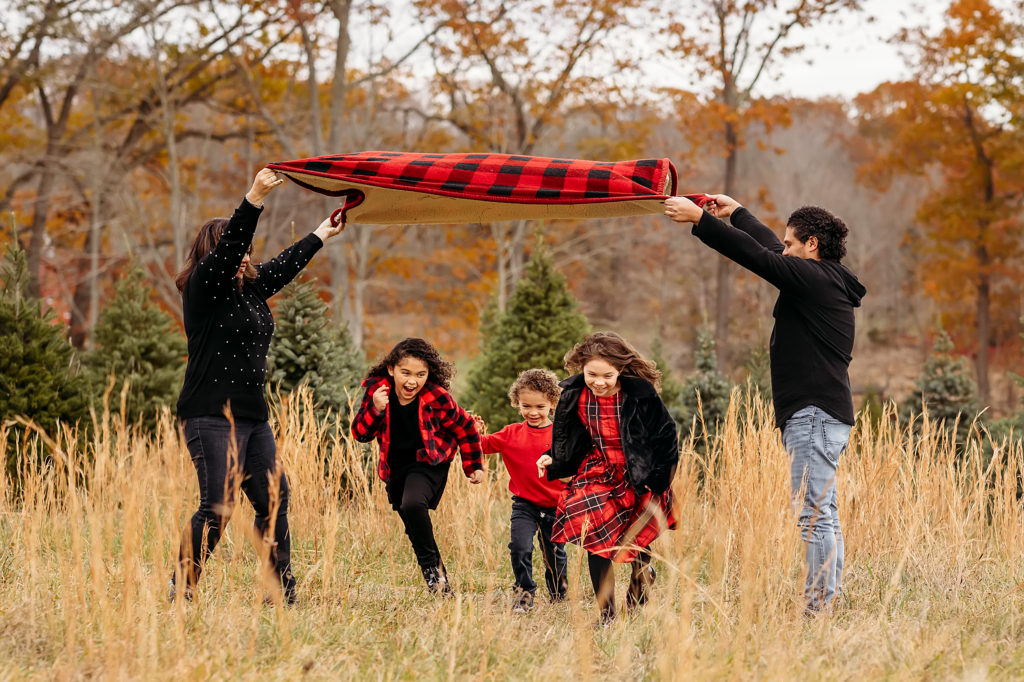 family with three children running underneath a blanket at a tree farm. CT photographer