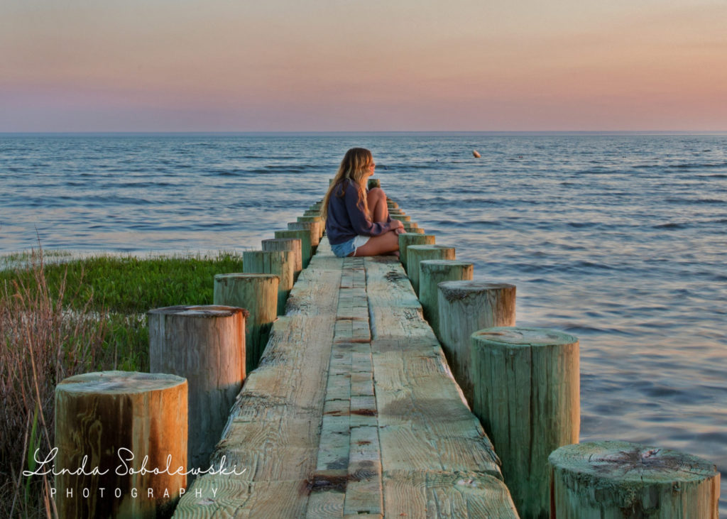 girl with long blonde hair sitting on a pier at the beach during sunset