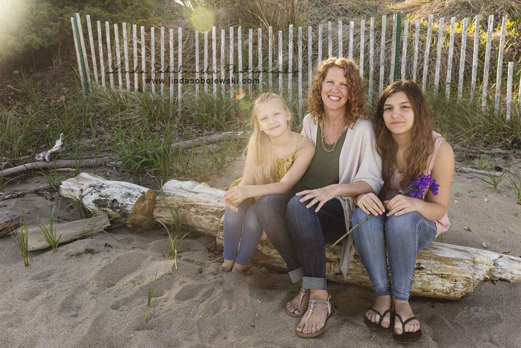 mother and her two daughters sitting on a log at the beach, Westbrook family photographer