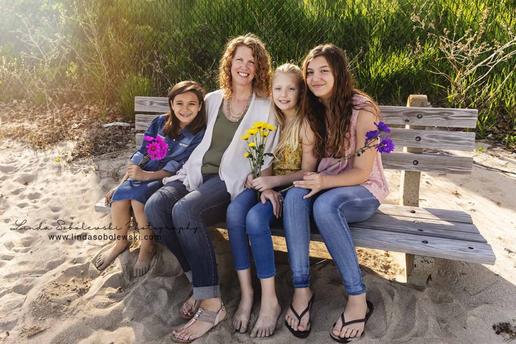 mom and three daughters sitting on a log at the beach, Westbrook family photographer