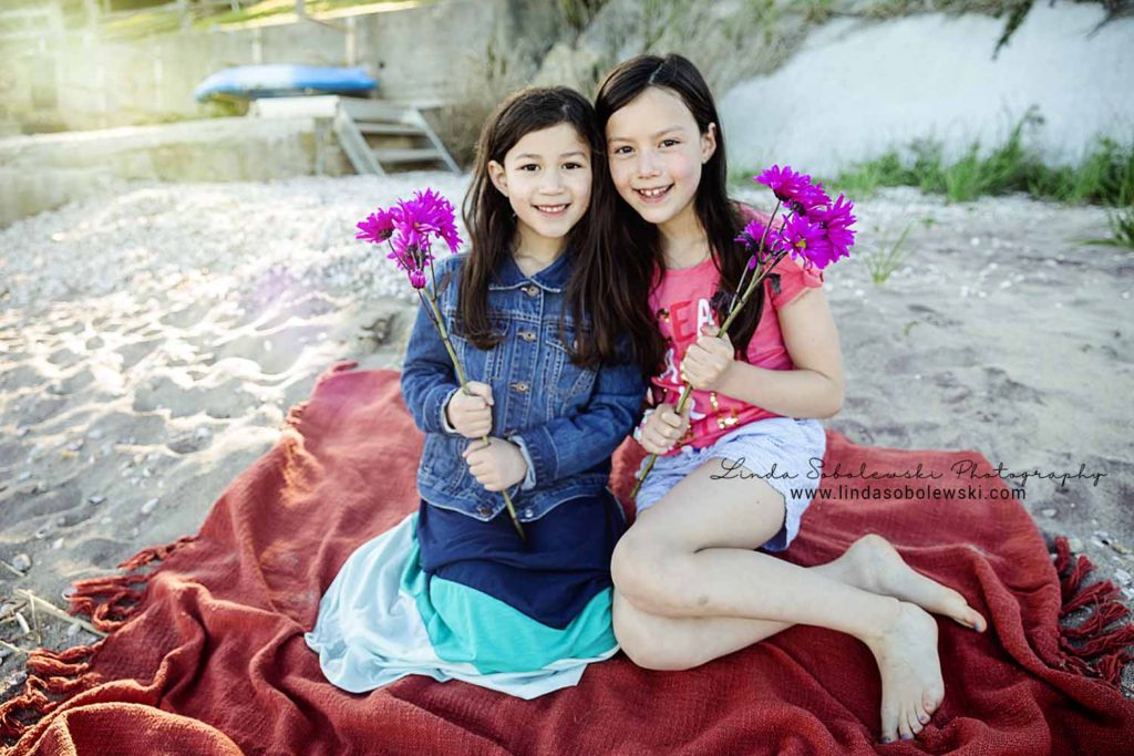 two little girls holding flowers, sitting on the beach, westbrook family session