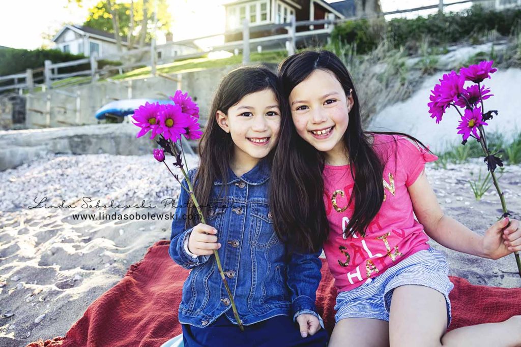 two little girls holding flowers, sitting on the beach, Westbrook family photographer