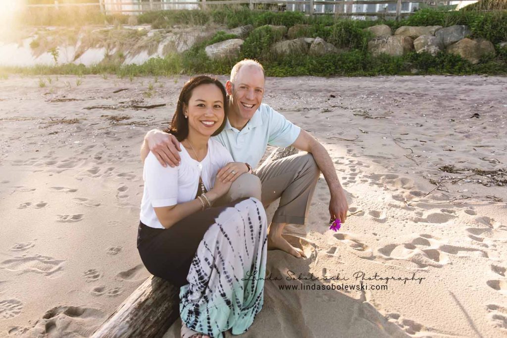 husband and wife sitting on a log on the beach, Connecticut shoreline photographer, family beach session