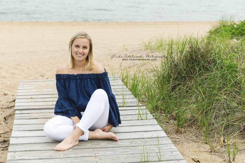pretty girl with blonde hair and dark top, sitting at the beach at the surf club in Madison, ct, senior photography