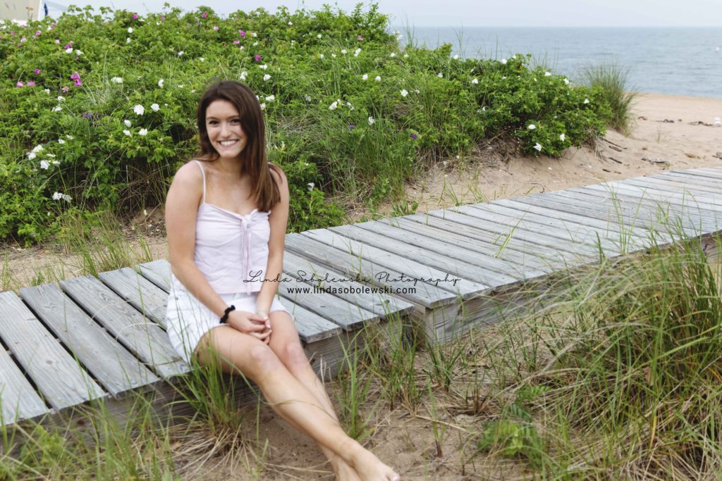 girl with dark hair and white tank top, sitting on a deck with greenery at the beach, Madison ct photographer