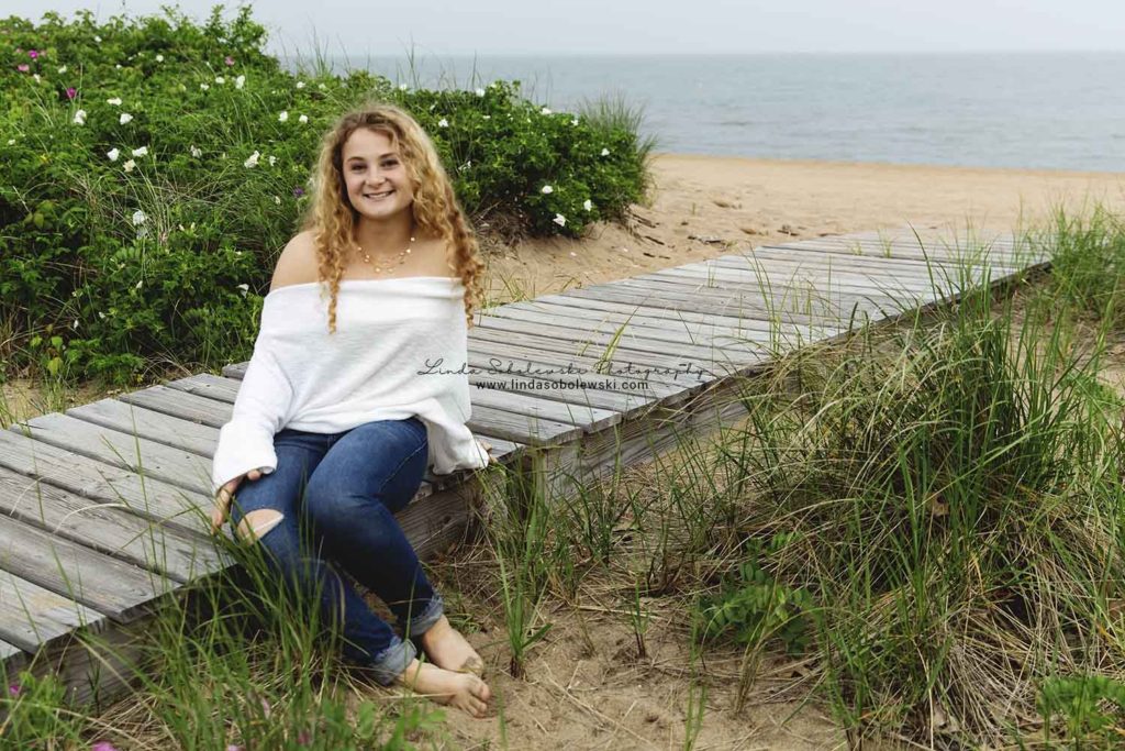 girl with blonde curley hair sitting on a wooden deck at the beach, Madison, ct senior photographer