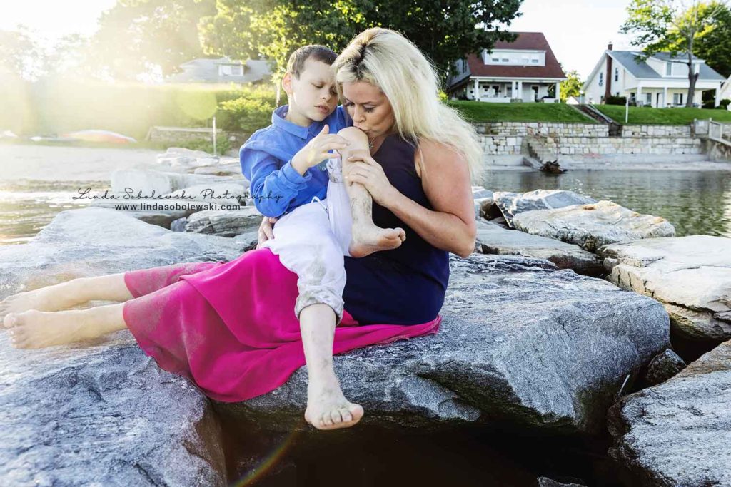 mother kissing her son's knee at the beach, old Saybrook ct family photographer