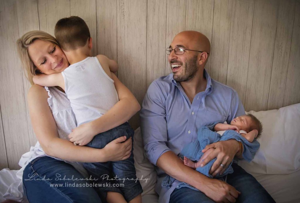 new family of four snugging in bed together, guilford new born photographer