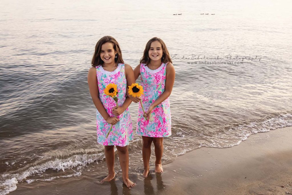 twin girls at the beach holding sunflowers during the sunset in Westbrook, CT, photo session