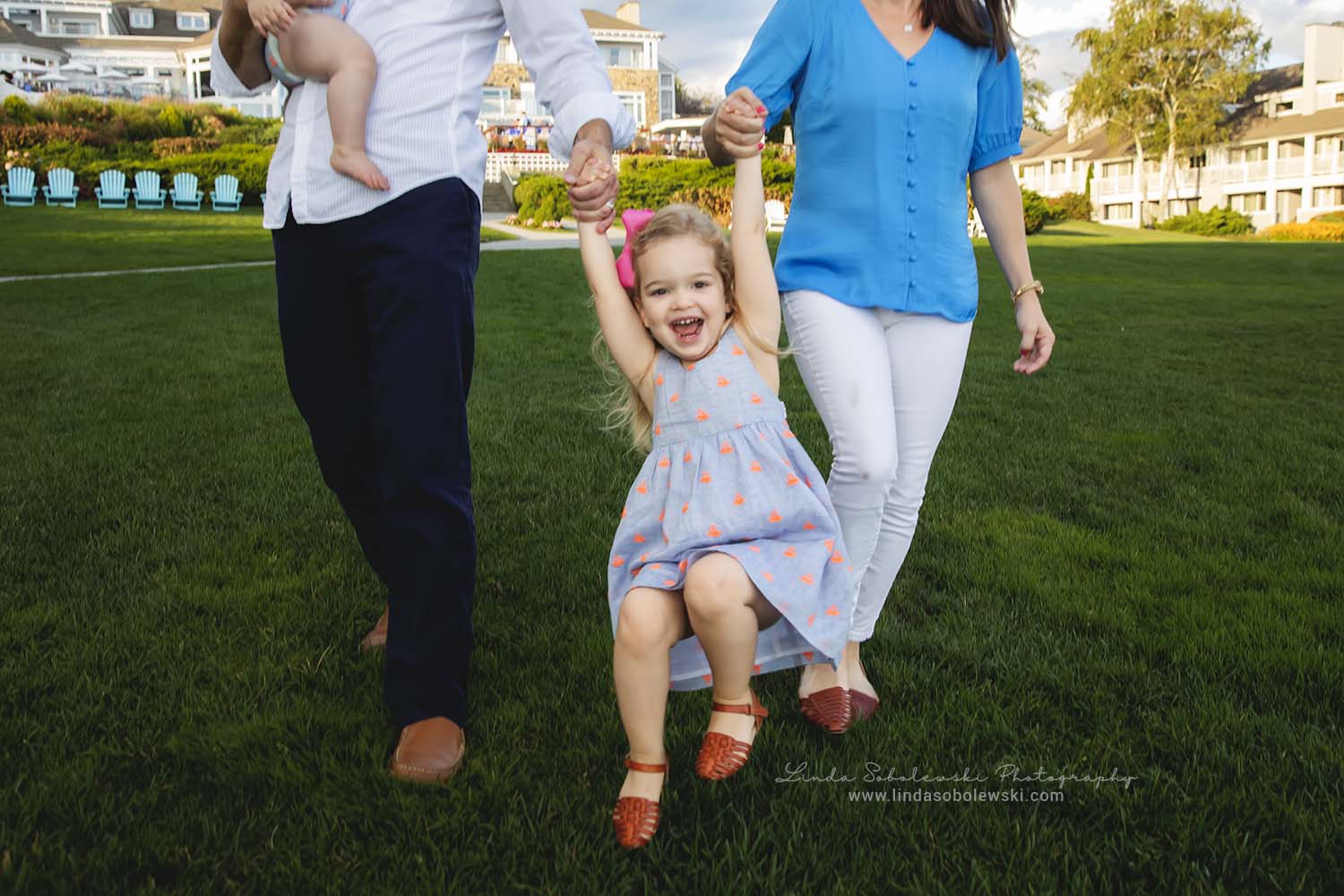 blonde little girl holding hands with her mom and dad, and laughing, family photo session in Westbrook, CT