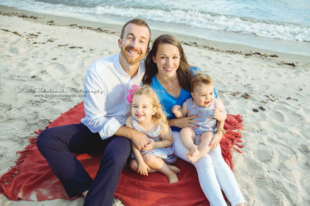family of four sitting on a red blanket at the beach, Westbrook CT family photographer