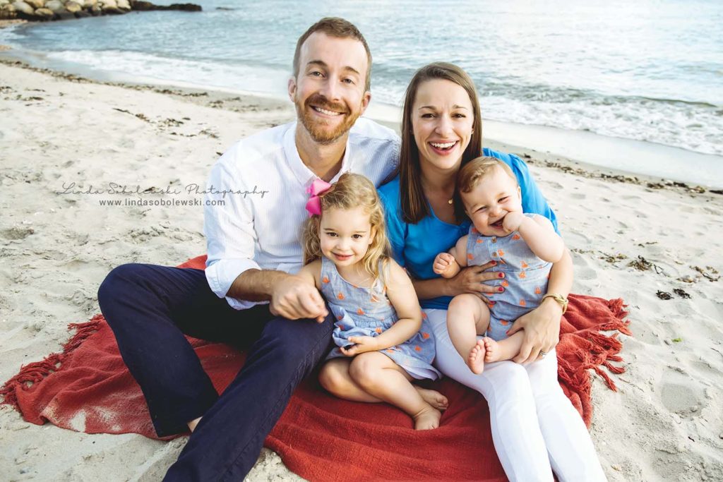 family of four sitting on a red blanket at the beach, Westbrook CT family photo session