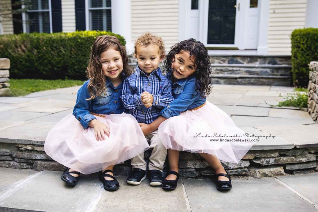 twin girls and their baby brother sitting on the front steps of their home, in Guilford, CT