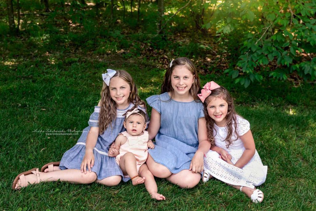 girls in dresses and bows sitting on the grass for spring backyard photos, Connecticut Lifestyle Photographer
