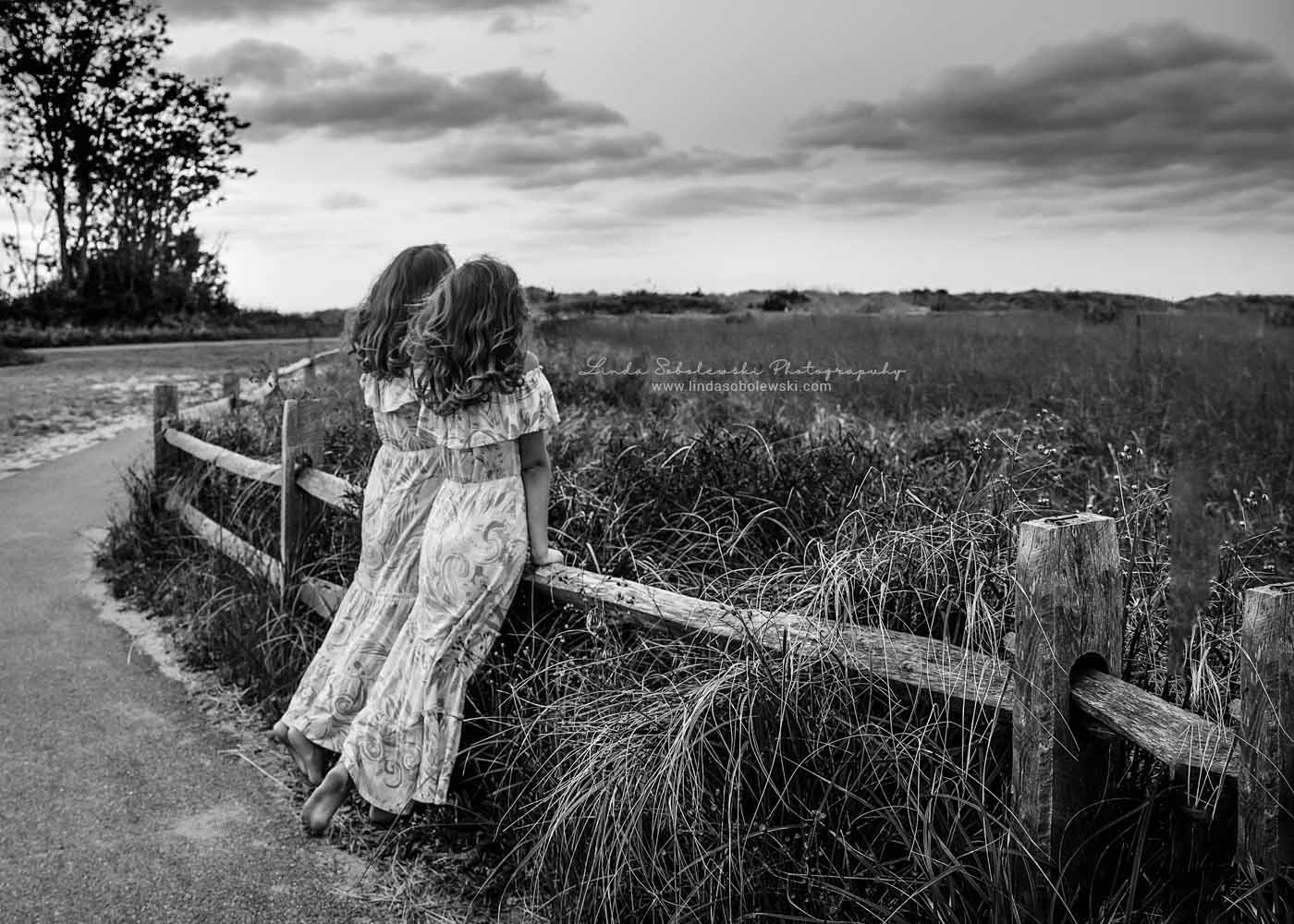 black and white image of two girls looking over a fence, Westbrook Photography session