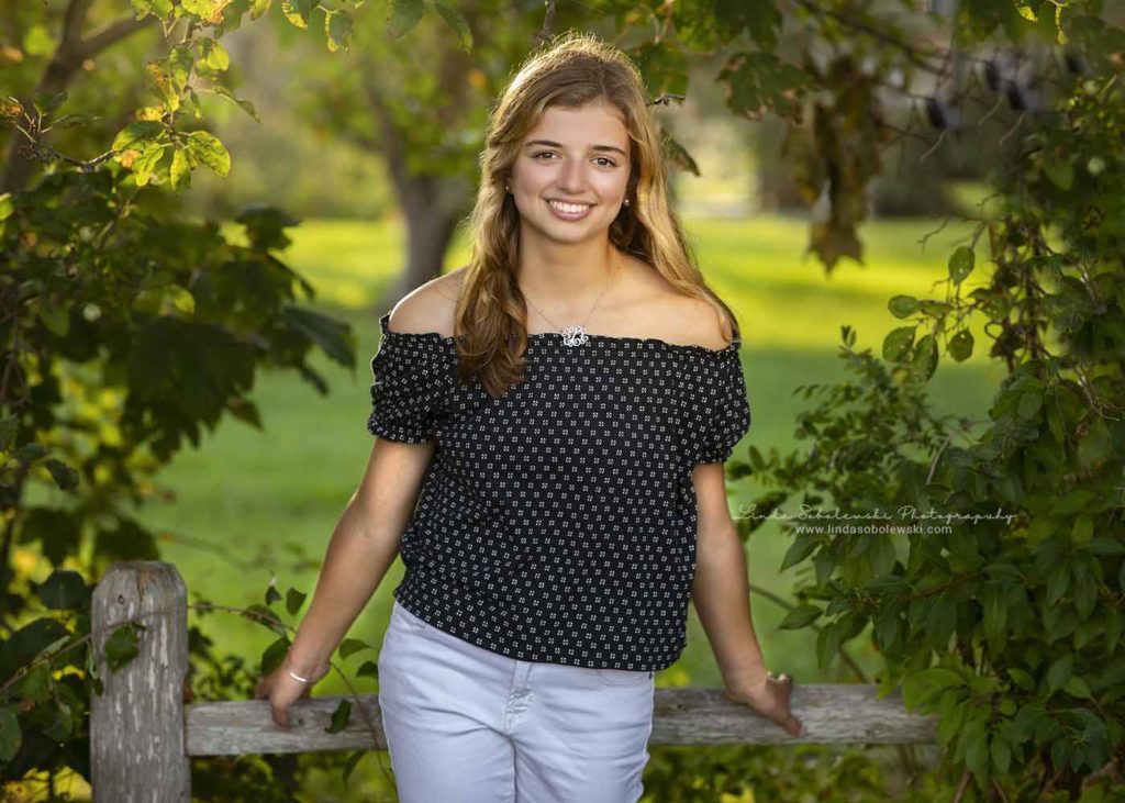blond girl in blue blouse, standing against a fence. CT's best High School Senior Photographer