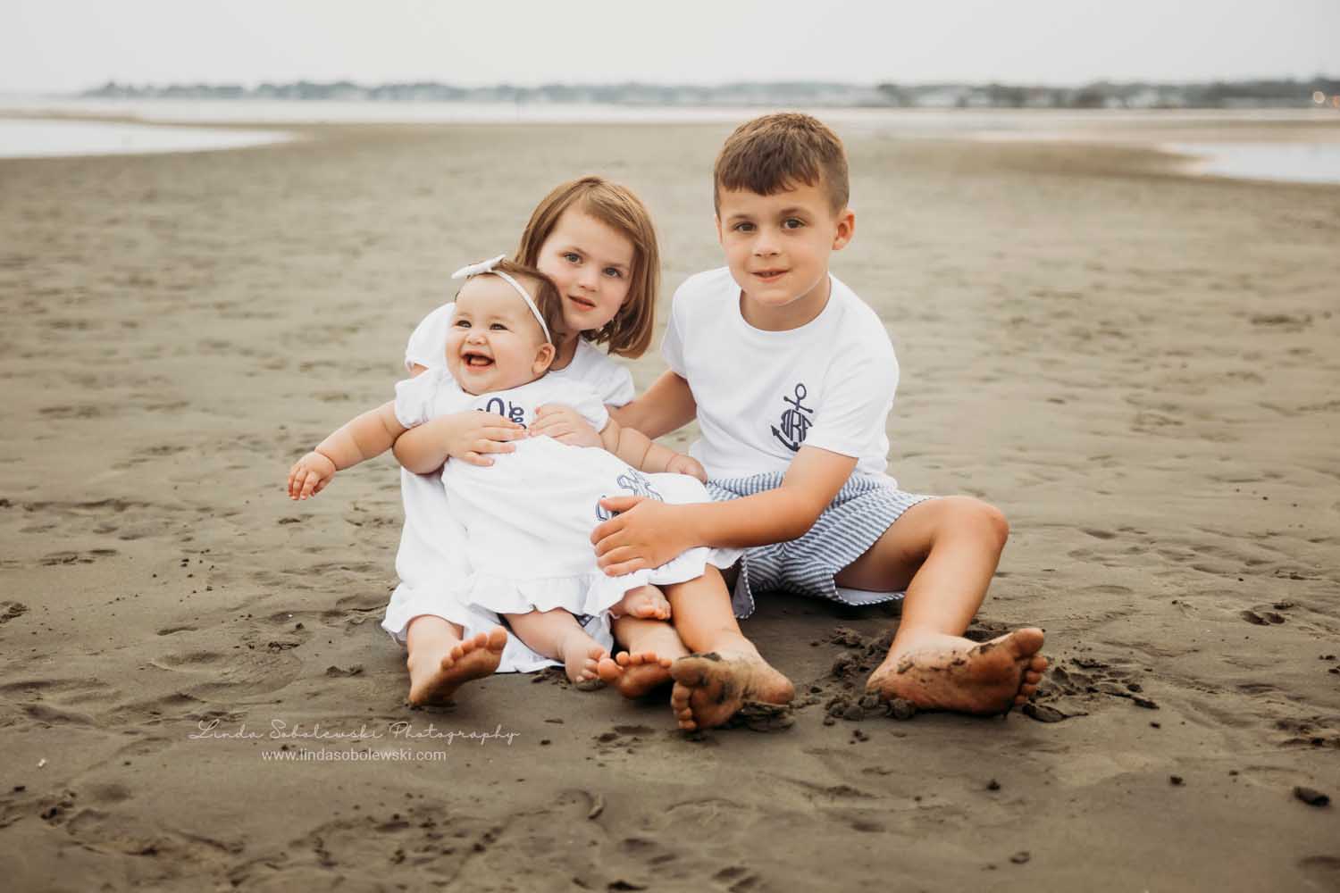 three children sitting in the sand at the beach, CT shoreline photographer