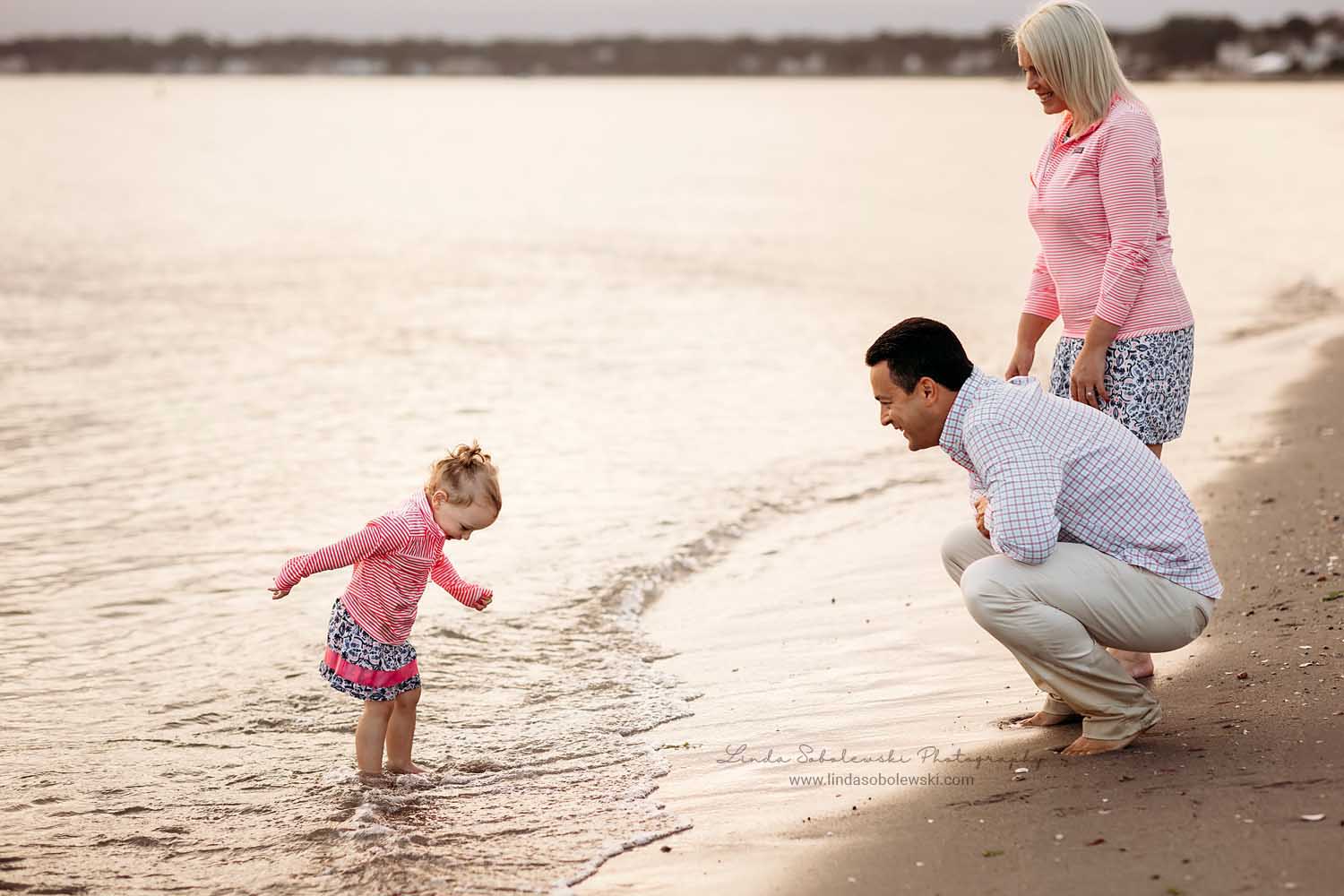 little girl in pink shirt and her family playing in the water, photo session at the beach, CT Shoreline Family photographer