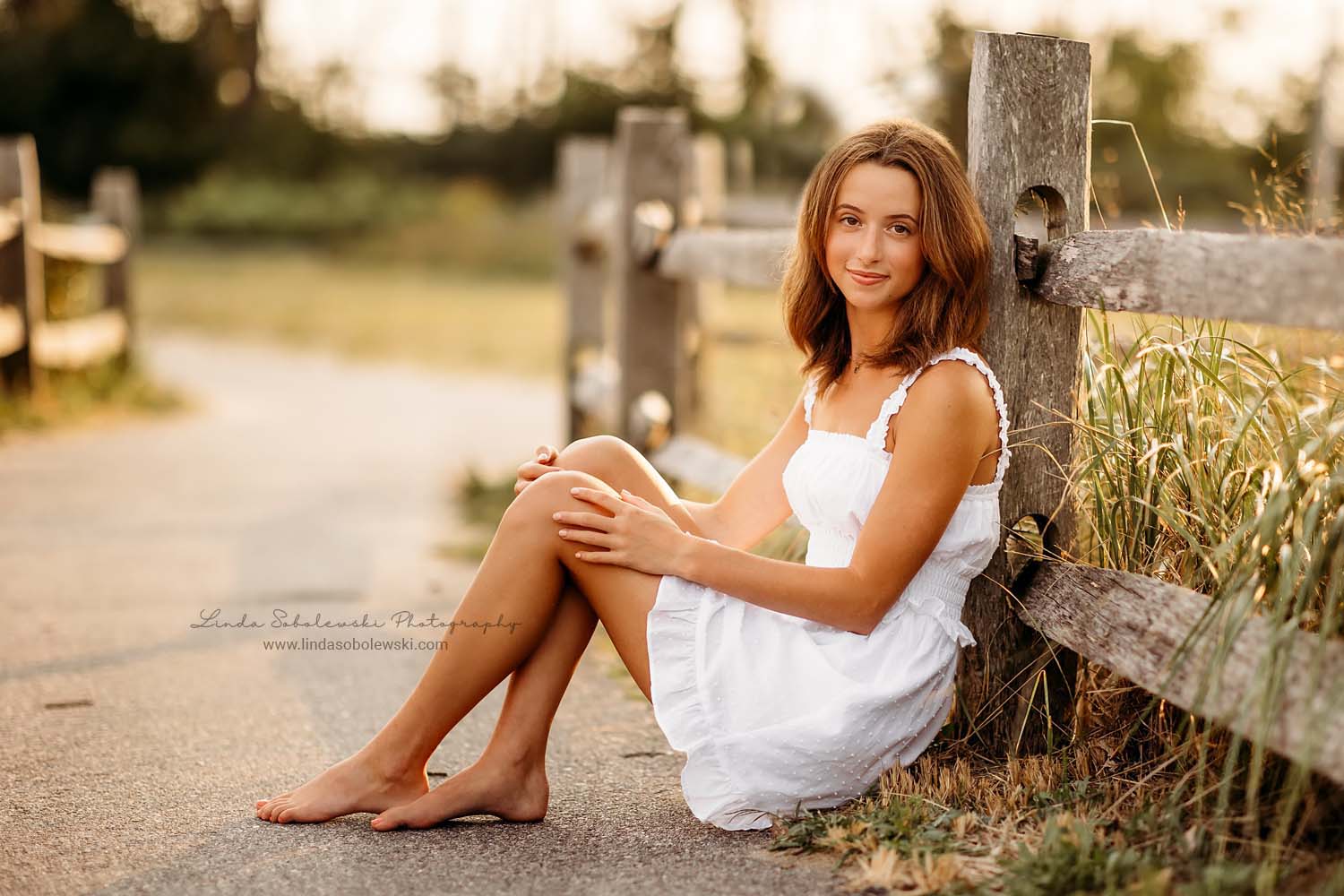 girl in white dress sitting against a fence, Madison CT senior photographer