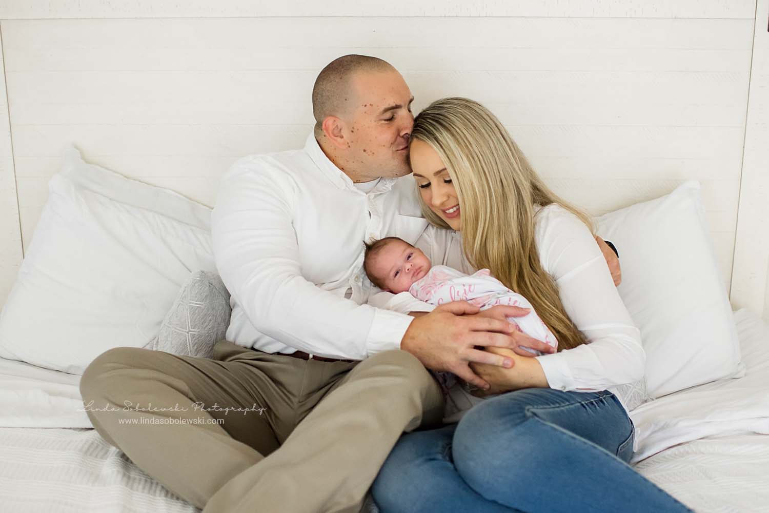 dad kissing mom on the forehead as she holds their newborn baby, Westbrook CT newborn photographer