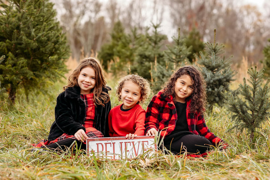 three children sitting in a tree farm holding a sign, Tree Farm photography sessions