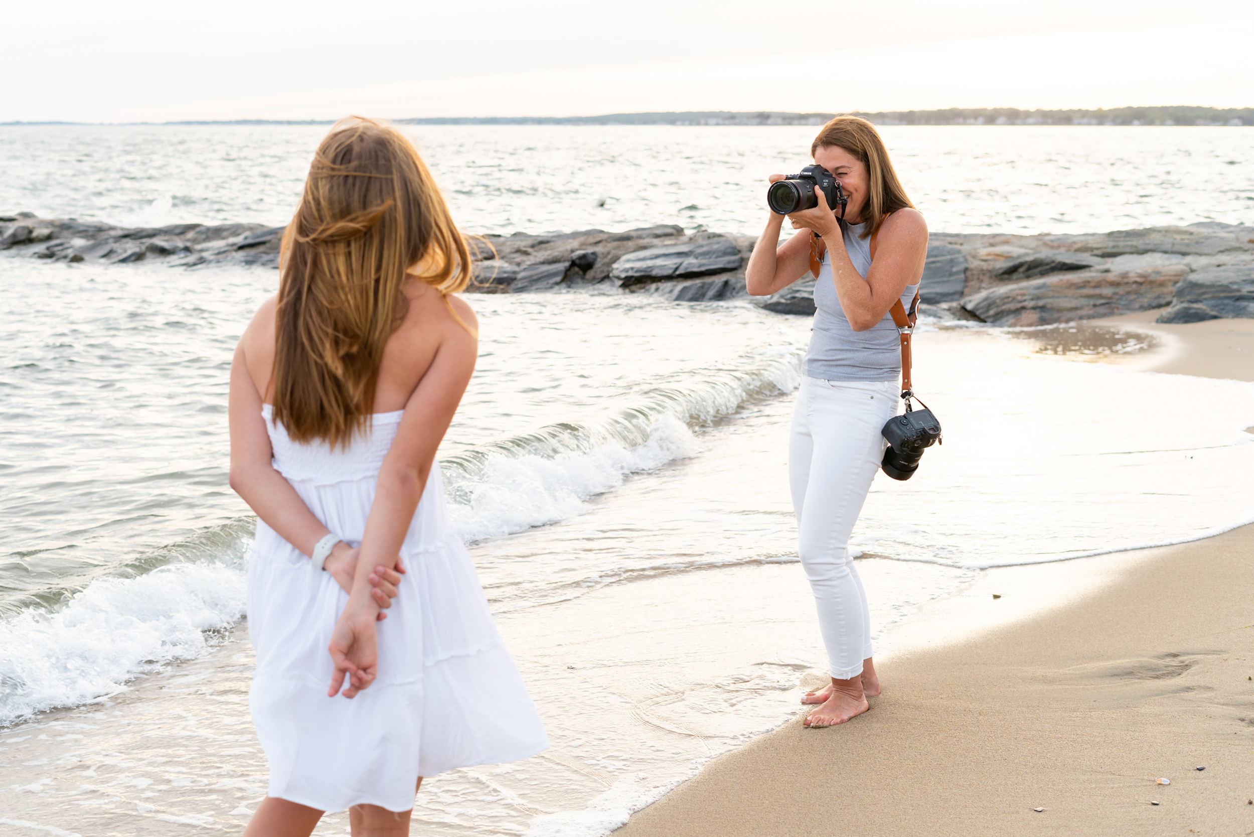 beautiful woman in white pants taking photos of a young girl on the beach, CT Best Senior, Family and Newborn Photographer