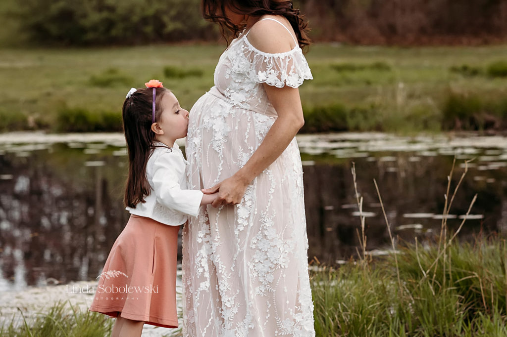little girl in pink dress kissing her mother's expectant belly, CT shoreline maternity photo session