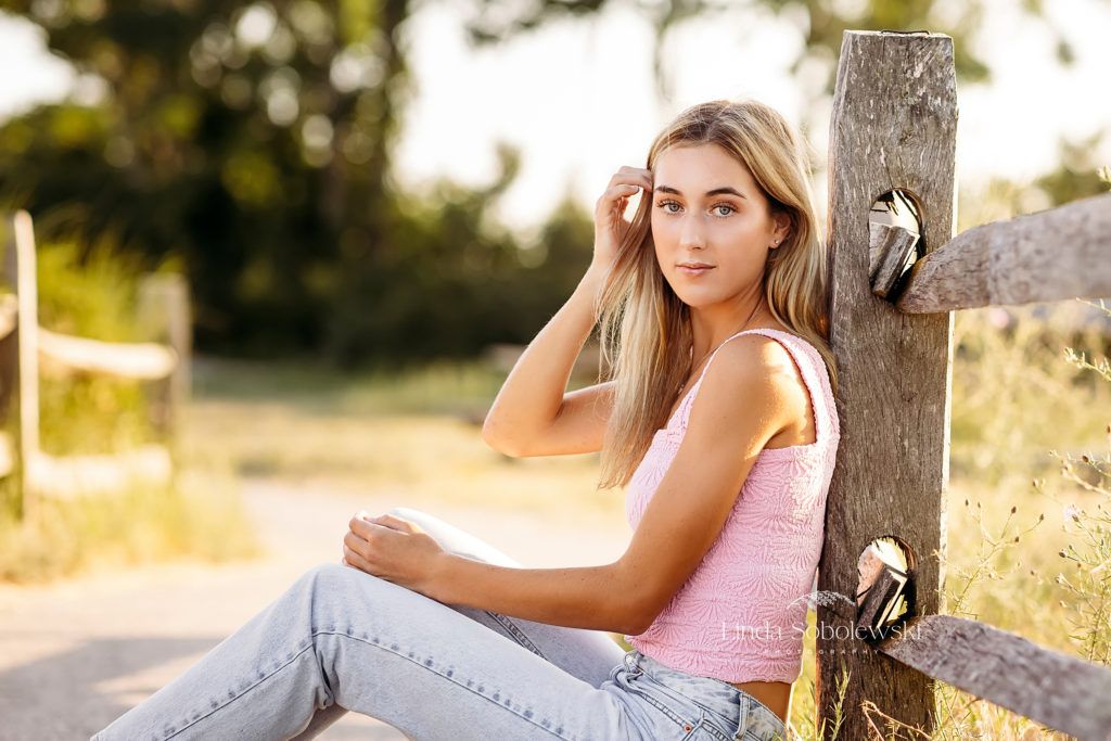 blonde girl in pink top sitting on a fence, Madison Beach Photographer in CT shoreline