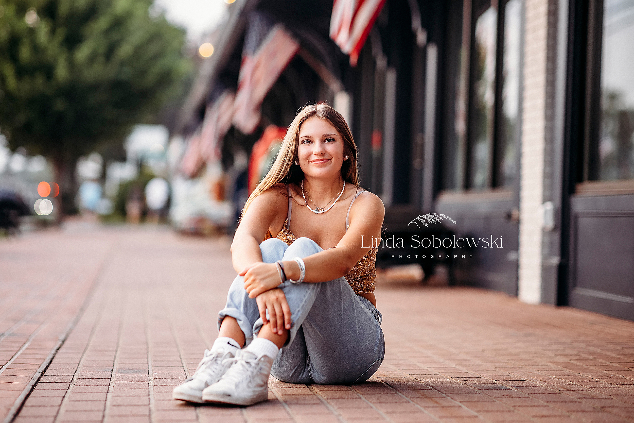 girl with long hair sitting on a sidewalk for an urban senior session in downtown Old Saybrook CT