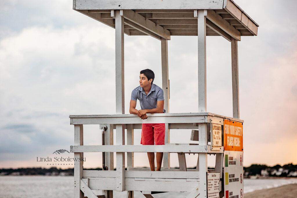 teenage boy standing on a lifeguard chair getting ready for a senior photo session at the beach, CT Senior photographer