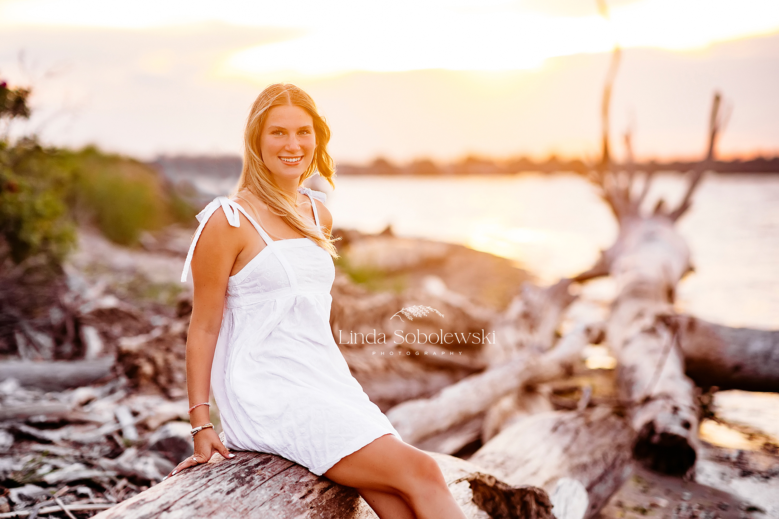 girl with blonde hair and white dress sitting on a log at the beach, CT Shoreline senior photographer