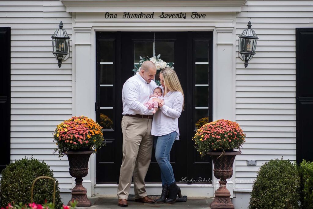 mother and father holding their newborn baby outside their home. Old Saybrook CT newborn photographer