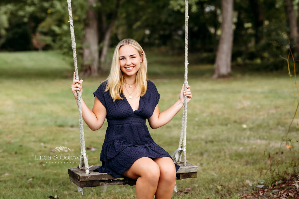 teenage girl with blonde hair and blue dress sitting on a wooden swing, Florence Griswold Museum senior and  family photographer