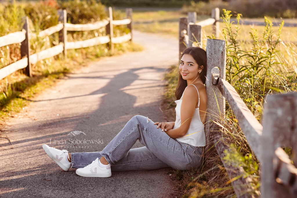 girl wearing white tank top and blue jeans sitting on a sidewalk, CT Senior photographer for a senior girl photo session