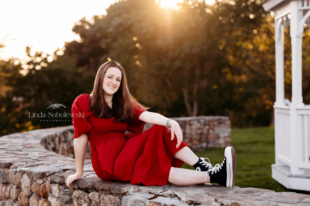 girl in red dress sitting on a stone wall at Founders Park in Old Saybrook CT, Westbrook senior photographer