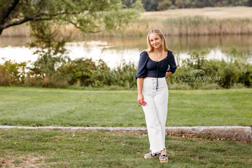 young girl in blue top and white pants standing in front of a river at the Florence Griswold Museum,Best Senior photographer in CT