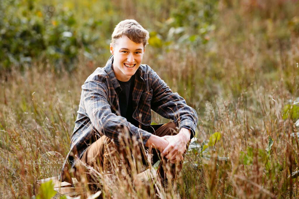 Hamden Hall high school senior boy in plaid shirt sitting in a field for his photo session, Madison CT Senior photographer