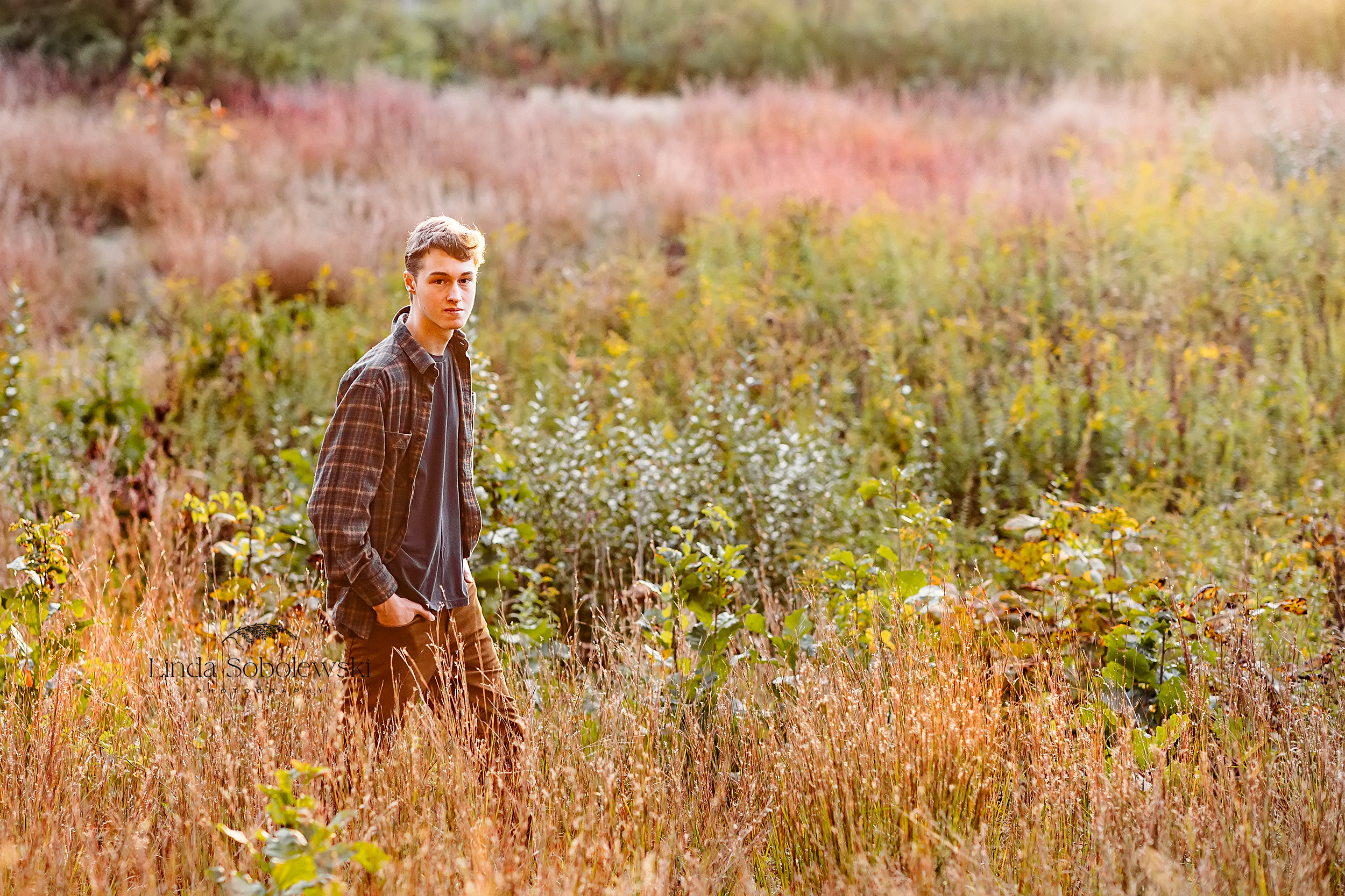 high school senior boy in plaid shirt sitting in a field, Madison CT Senior photographer