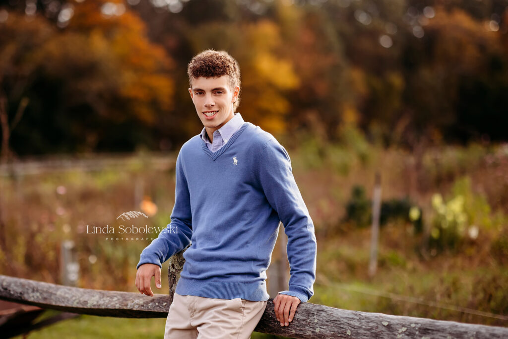 boy in blue sweater leaning against a fence, Madison CT Senior photographer