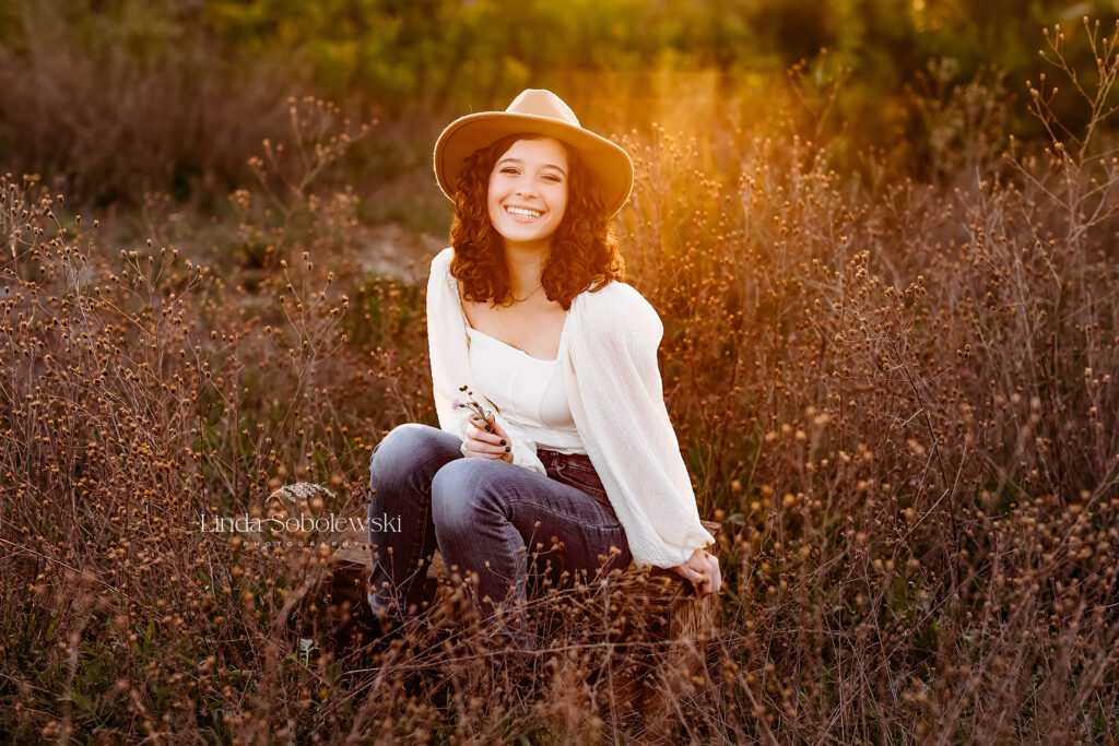 girl in white top and a hat sitting in a field with pretty light, Senior Photo session at Bauer Park in Madison CT