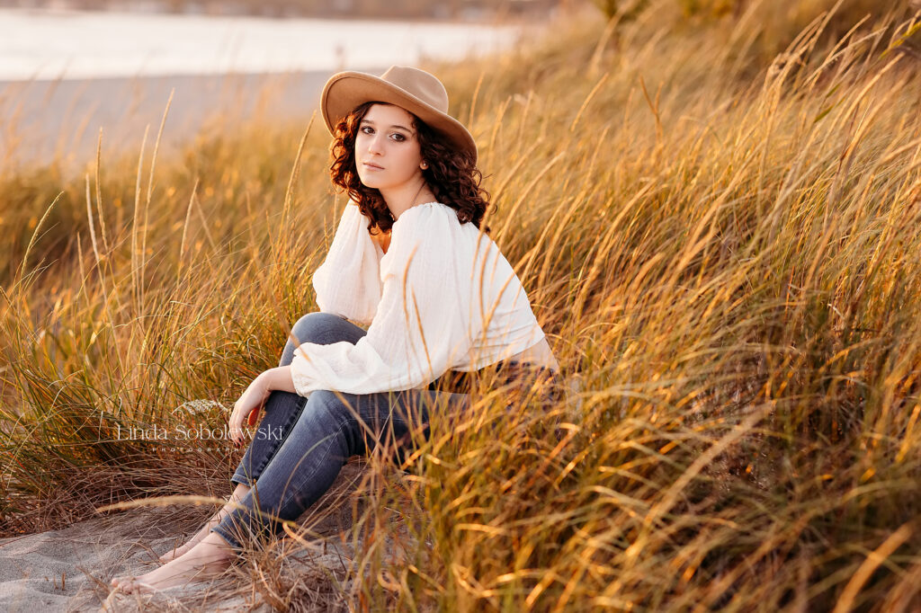 girl in white top and hat, sitting in grass at the beach, CT Beach photographer