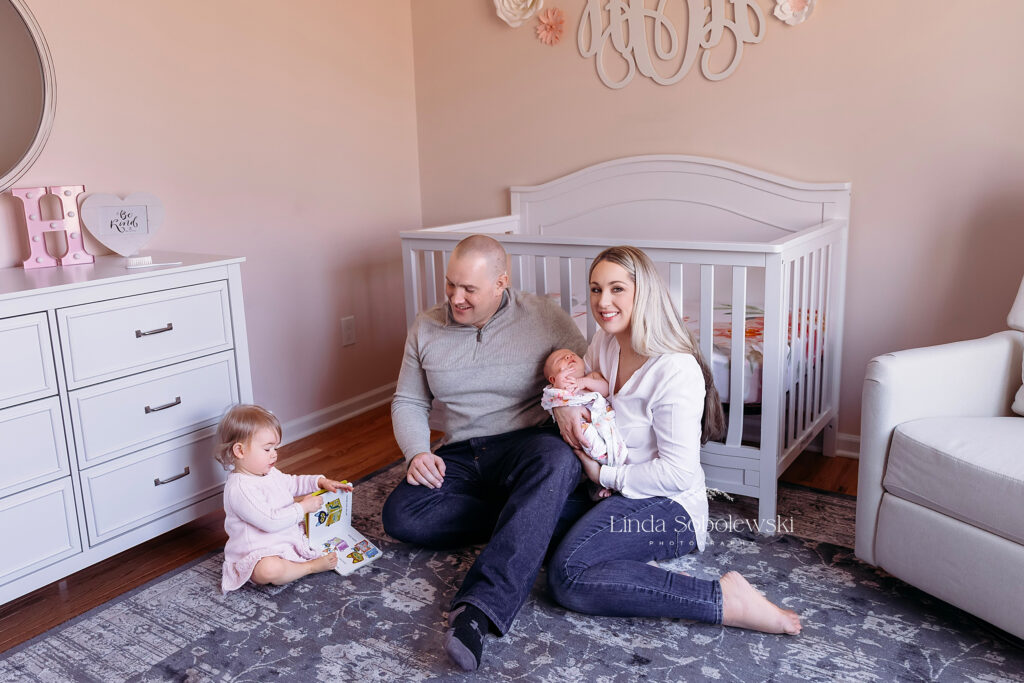 Family of four sitting on the floor of a baby's nursery, Madison CT photographer specializing in newborns