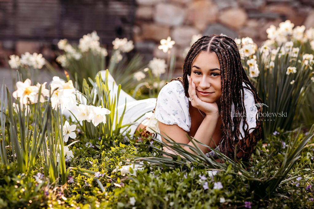 girl in white flowered top laying in the flowers at Elizabeth State Park in West Hartford, CT, Best Senior photographer in CT